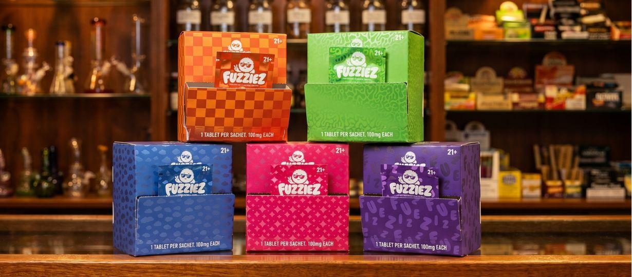 Is Fuzziez Legal in All 50 States? Fuzziez botanical relaxation tablet boxes displayed on a bar — Apple, Blue Razz, Pineapple, Strawberry, Mango, Berry flavors
